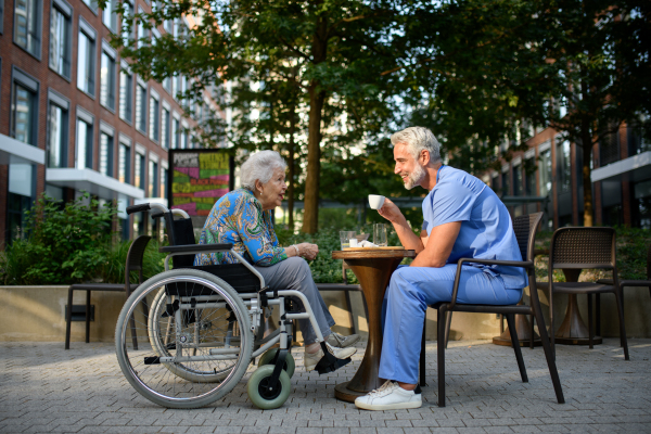Male nurse having a cup of coffee with senior patient in a wheelchair at a cafe.