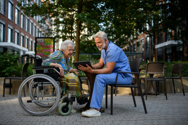 Male caregiver looking at photos in tablet with senior woman in a wheelchair.