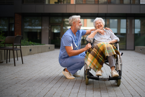Male caregiver pushing senior woman in a wheelchair.