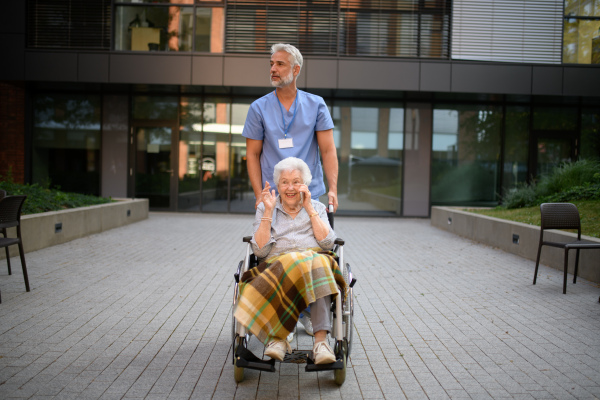 Male caregiver pushing senior woman in a wheelchair.
