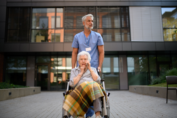 Male caregiver pushing senior woman in a wheelchair.