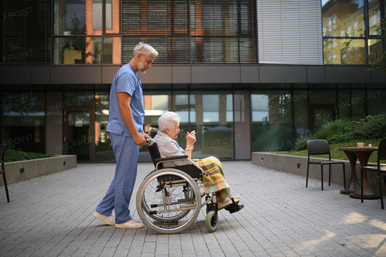 Side view of male caregiver pushing senior woman in a wheelchair.