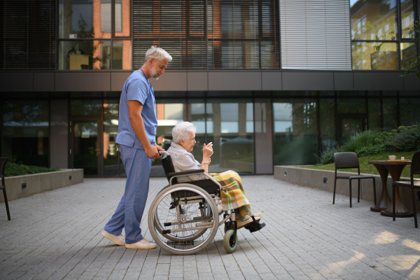 Side view of male caregiver pushing senior woman in a wheelchair.