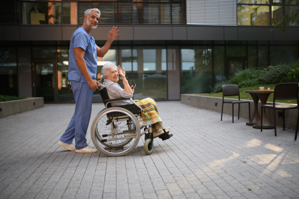 Male caregiver pushing senior woman in a wheelchair.