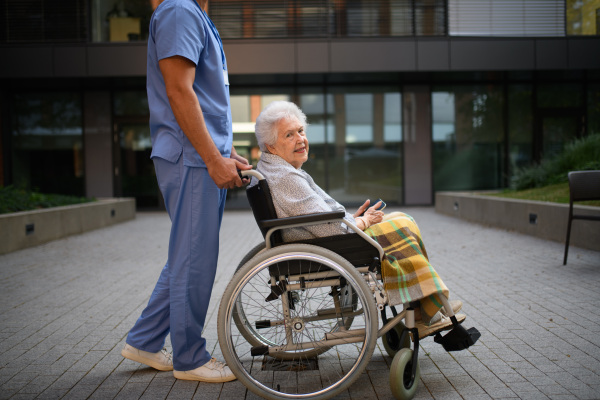 Side view of caregiver pushing senior woman in a wheelchair.