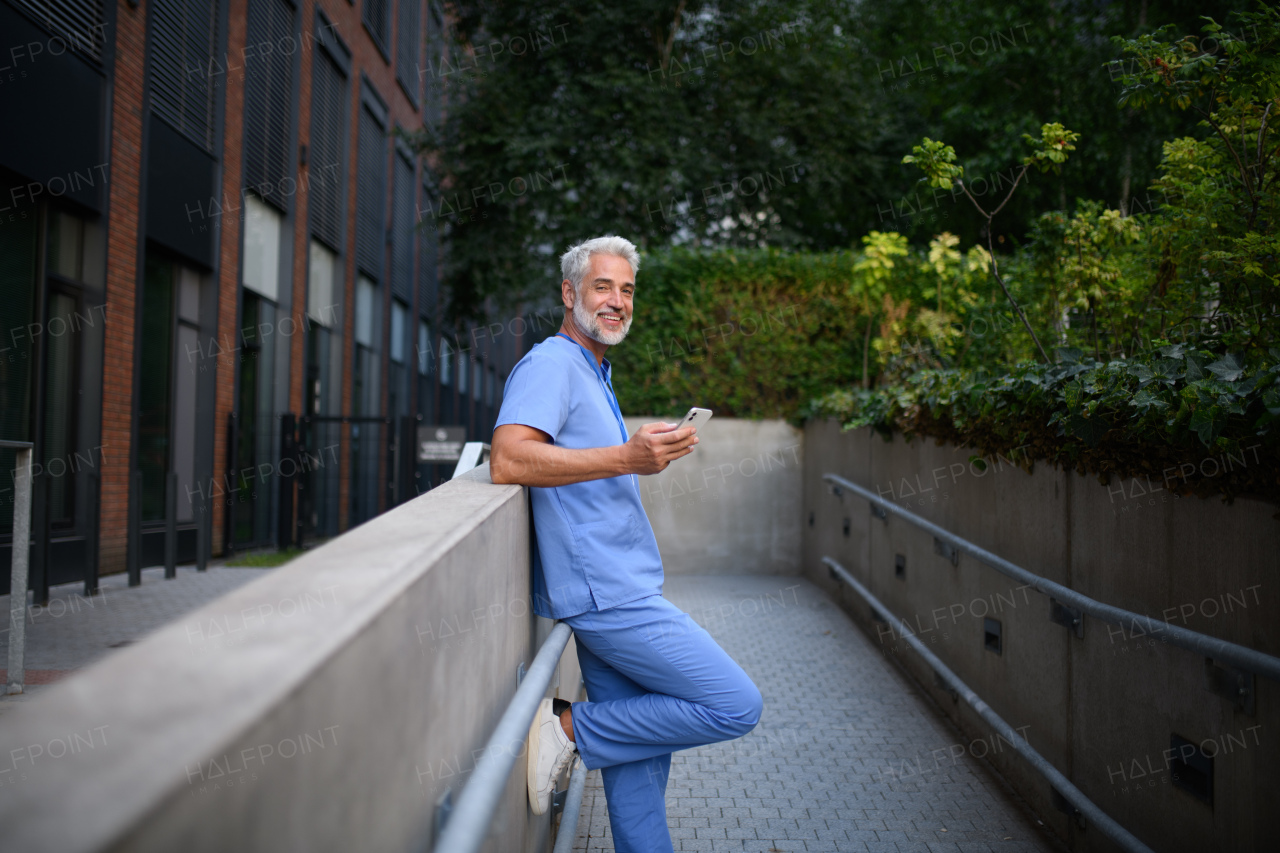 Healthcare worker in scrubs sitting outside hospital and checking phone during break.