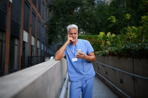 Healthcare worker in scrubs sitting outside hospital and checking phone during break.