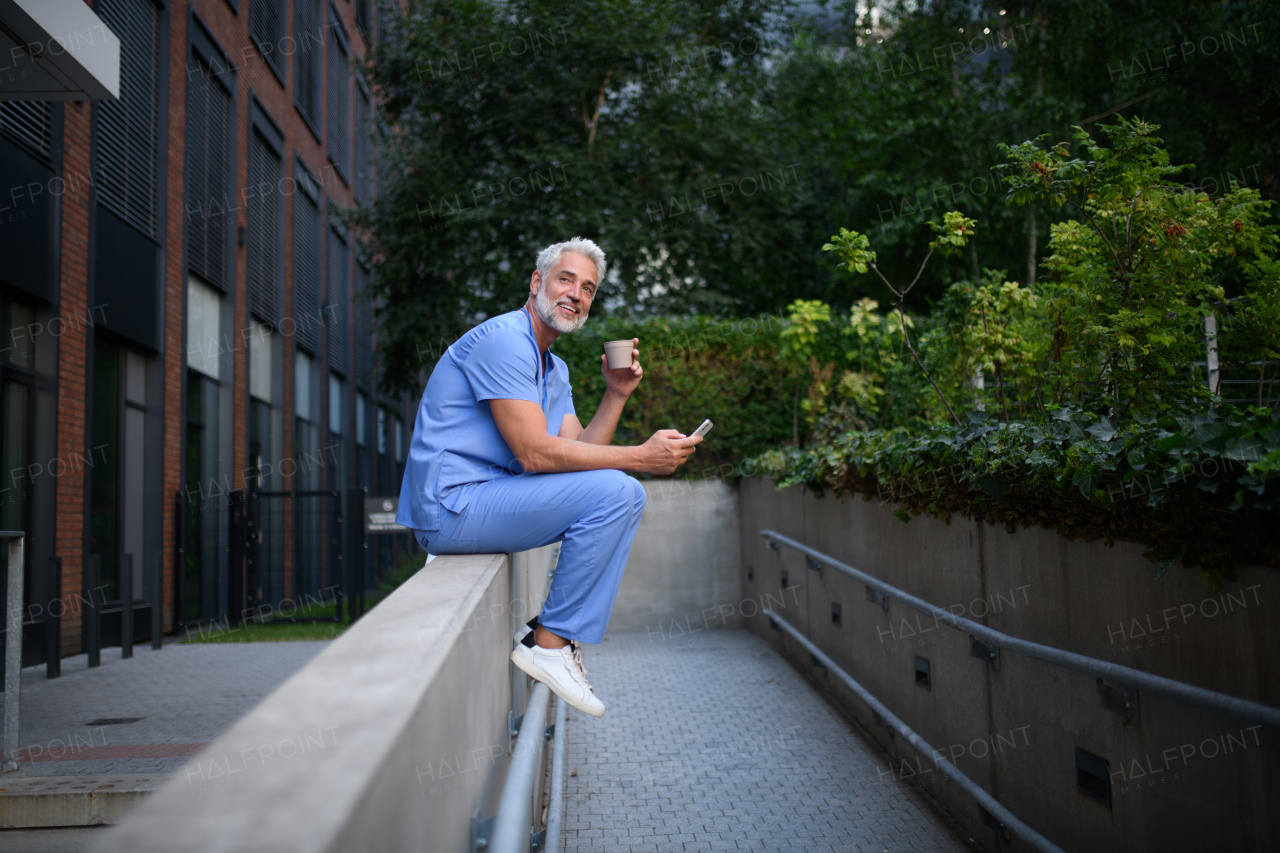 Healthcare worker in scrubs sitting outside hospital and checking phone during break.