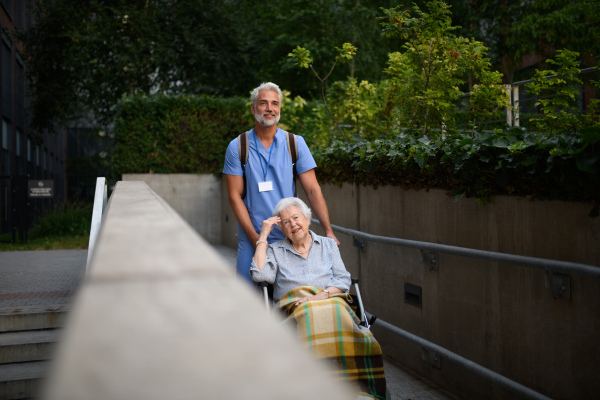 Male caregiver pushing senior woman in a wheelchair.