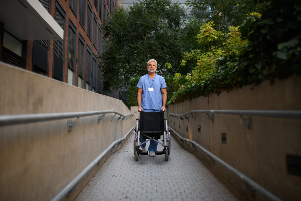 Portrait of handsome male caregiver pushing empty wheelchair.