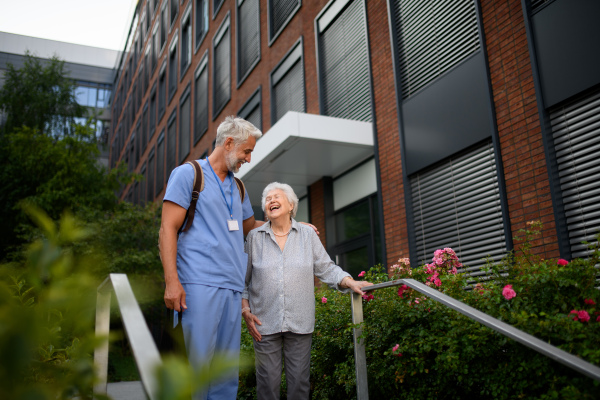 Caring healthcare worker helping elderly woman walk down the stairs.