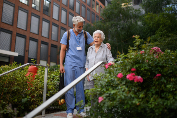 Caring healthcare worker helping elderly woman walk down the stairs.