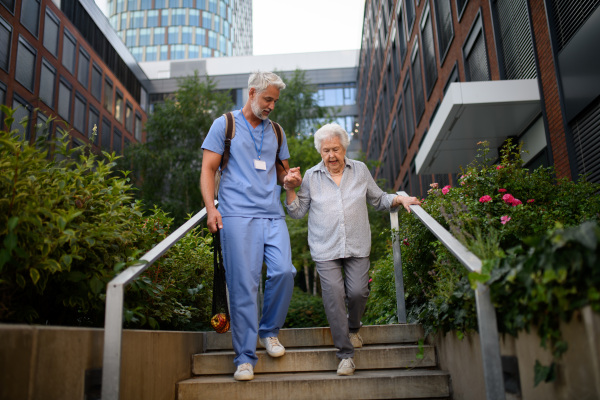 Caring healthcare worker helping elderly woman walk down the stairs.