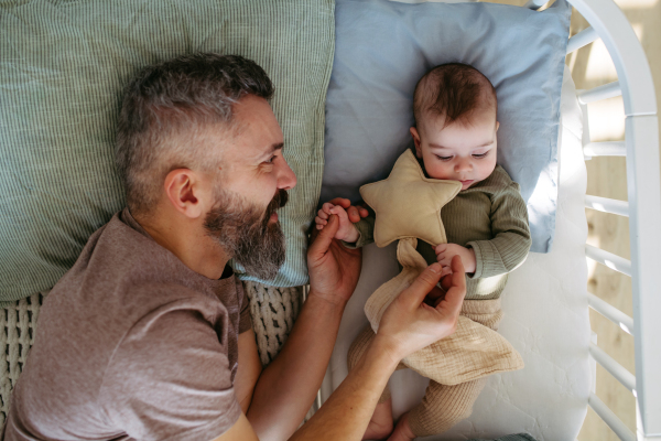 Father putting the baby to sleep, lying next to him in the crib and soothing him.