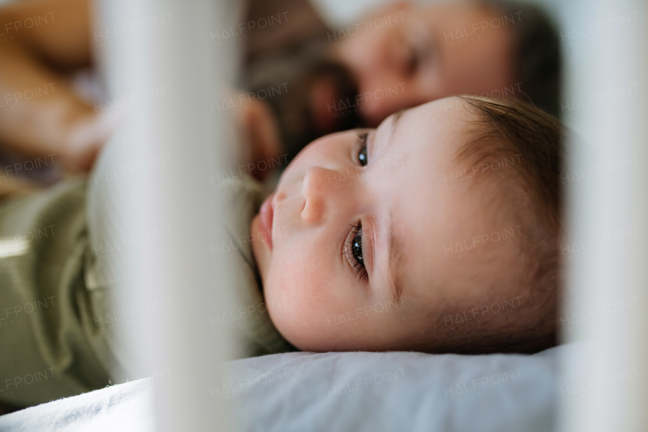 Father putting the baby to sleep, lying next to him in the crib and soothing him.