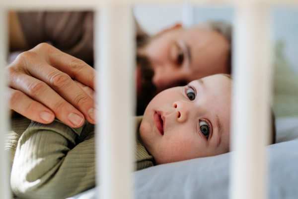 Father putting the baby to sleep, lying next to him in the crib and soothing him.