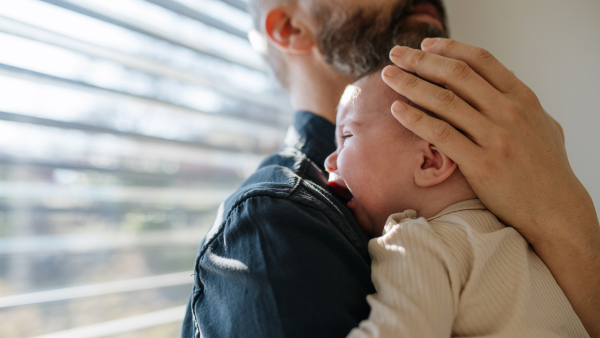 Father comforting his crying baby son, holding him in arms.