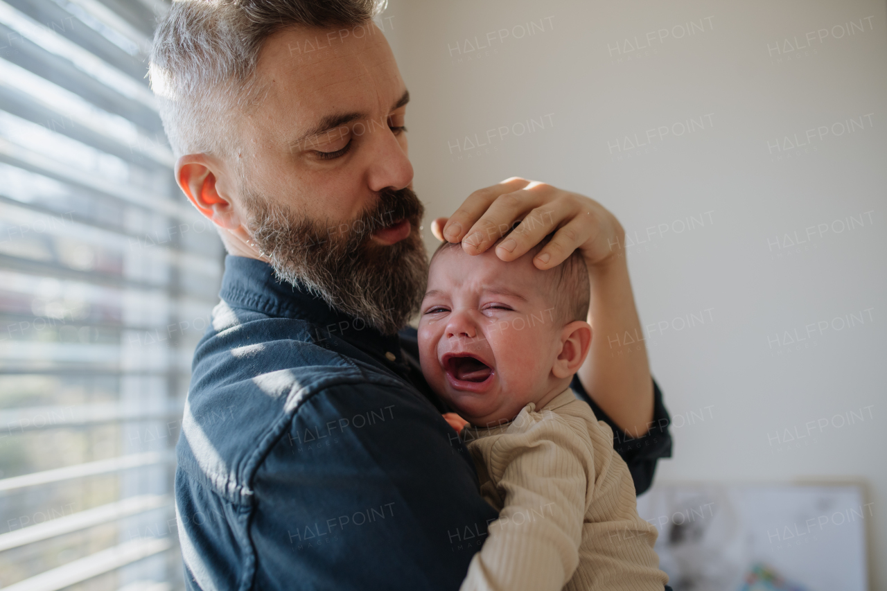 Father comforting his crying baby son, holding him in arms.