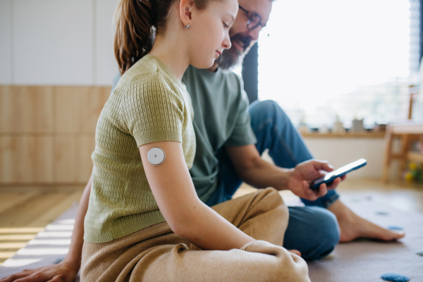 Diabetic girl with a CGM sensor on her arm. Father using an app to monitor blood sugar levels.