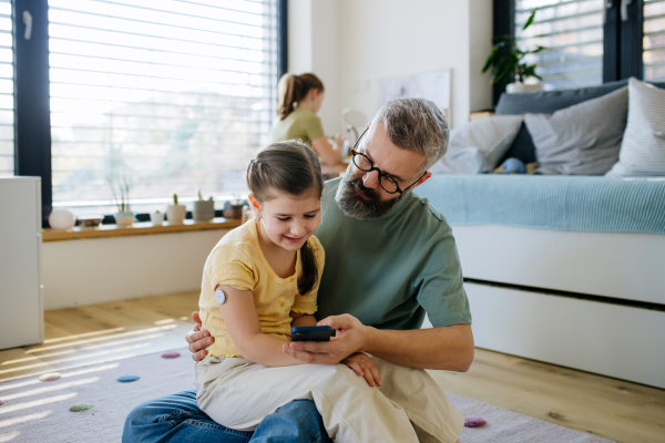 Diabetic girl with a CGM sensor on her arm. Father using an app to monitor blood sugar levels.