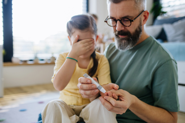 Father assisting his daughter with a blood sugar test at home.