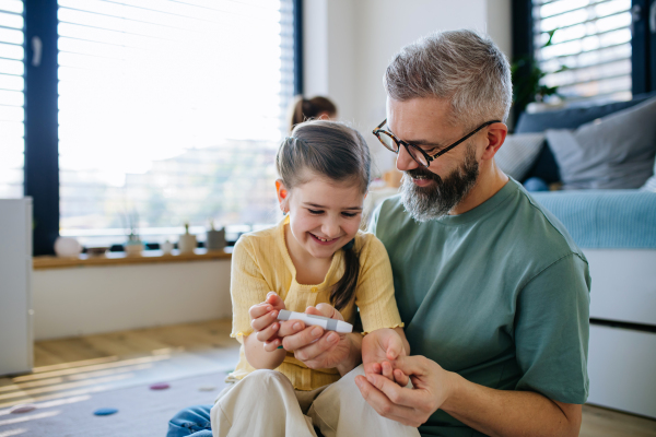 Diabetic girl taking blood sugar test at home, father helping.