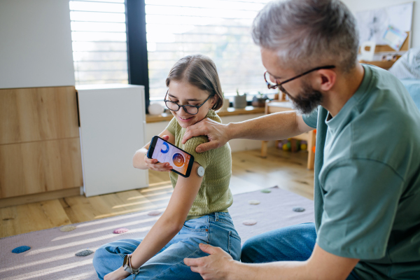 Diabetic girl with a CGM sensor on her arm. Father using an app to monitor blood sugar levels.