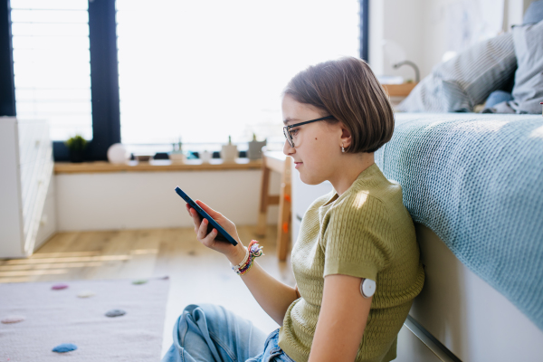 Diabetic girl with CGM sensor checking her blood sugar level in app.