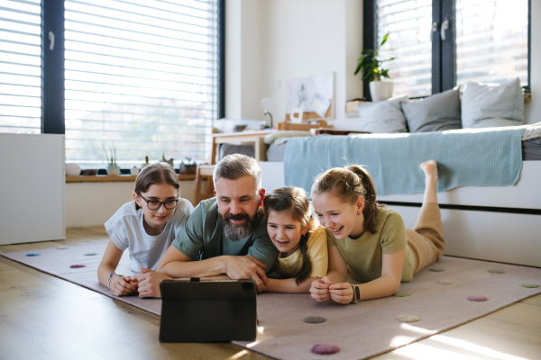 Portrait of father with three daughters watching tv show on tablet. Girl dad concept.
