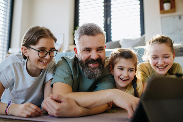 Portrait of father with three daughters watching tv show on tablet. Girl dad concept.