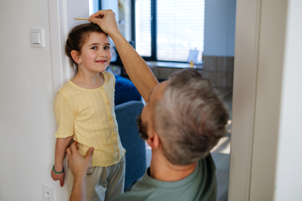 Father measuring his daughter's height at home, making line on doorframe.