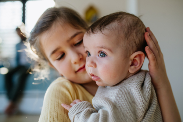 Big sister comforting sad baby brother, holding him in arms.