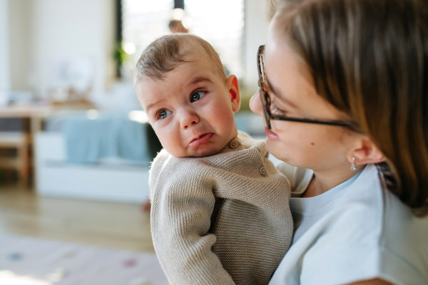Big sister comforting crying baby brother, holding him in arms.