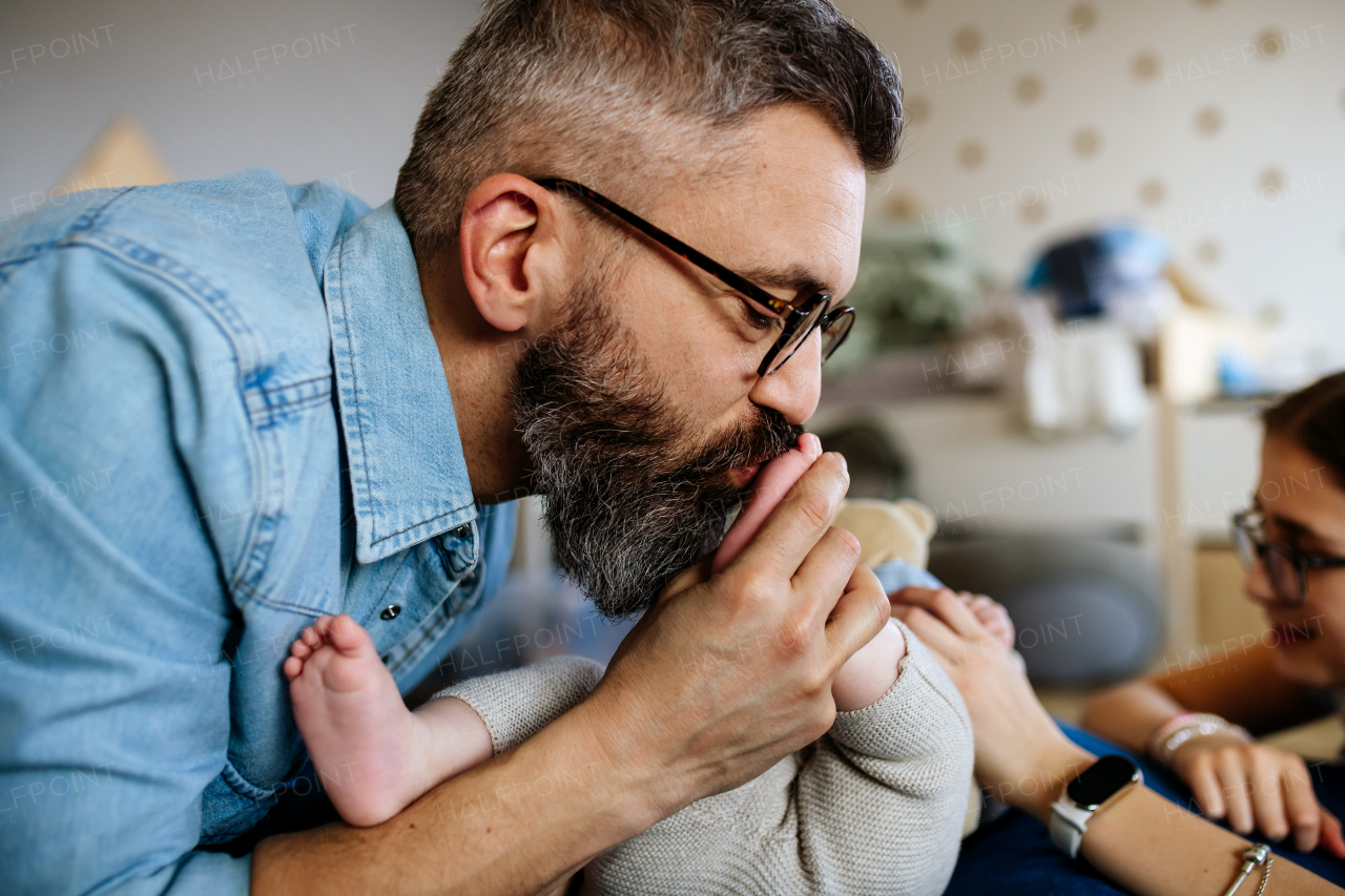 Portrait of father kissing little baby boy's feet. Side view.