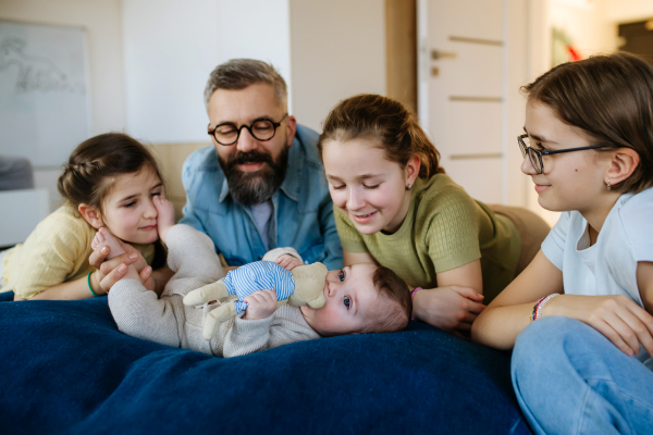 Three sisters looking at newborn brother in fathers arms. Big family concept.