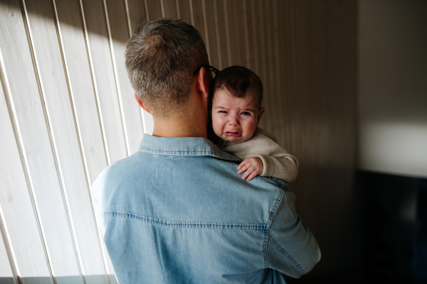 Father comforting his crying baby son, holding him in arms.