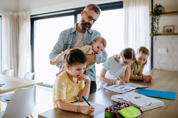 Father helping his daughters with homework while taking care of baby. Big family.