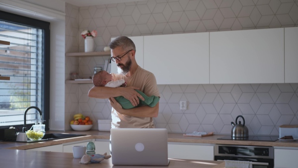 Father comforting his baby son while working, holding him in arms.