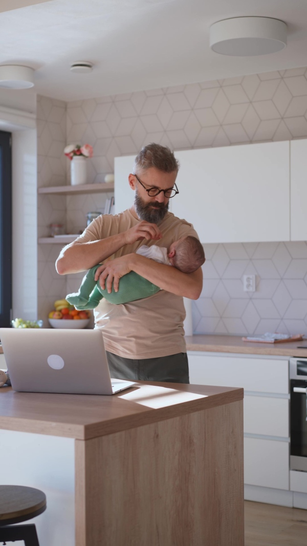 Father comforting his baby son while working, holding him in arms.