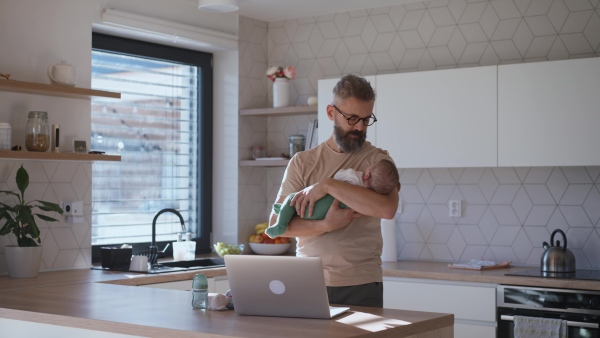 Father comforting his baby son while working, holding him in arms.