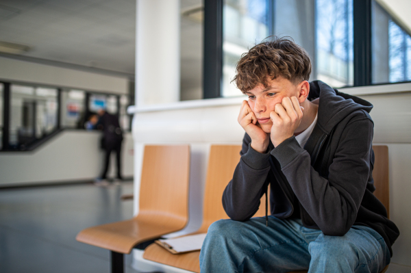 Anxious male teenager waiting alone in hospital waiting area before preventive medical checkup.