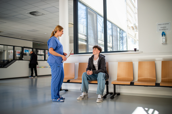 Friendly doctor talking with teenage patient in hospital hallway.