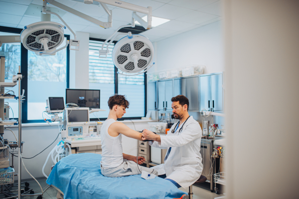 Teen boy undergoing medical checkup with smiling doctor in hospital room.