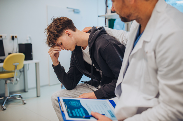 Close-up of doctor and teenage patient filling out mental health evaluation form together.