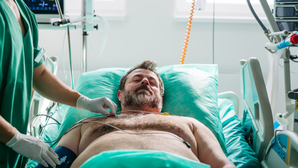 Doctor placing ECG electrodes on male patient in hospital bed