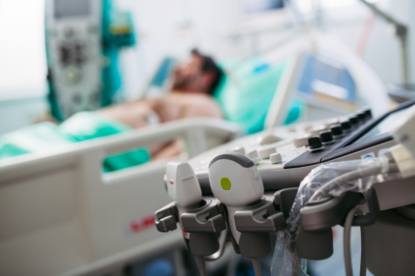 Ultrasond console in hospital, patient in hospital bed behind.