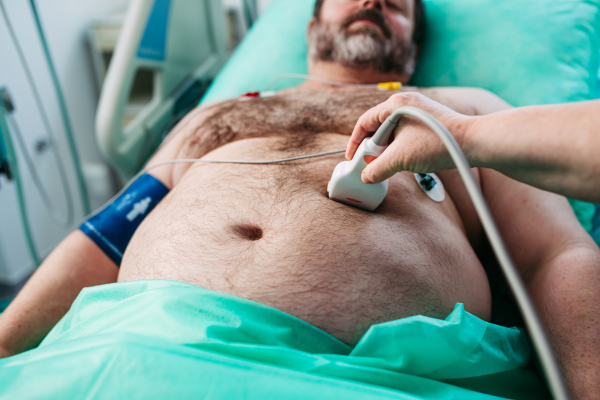 Close-up of doctor performing abdominal ultrasound on ICU patient.
