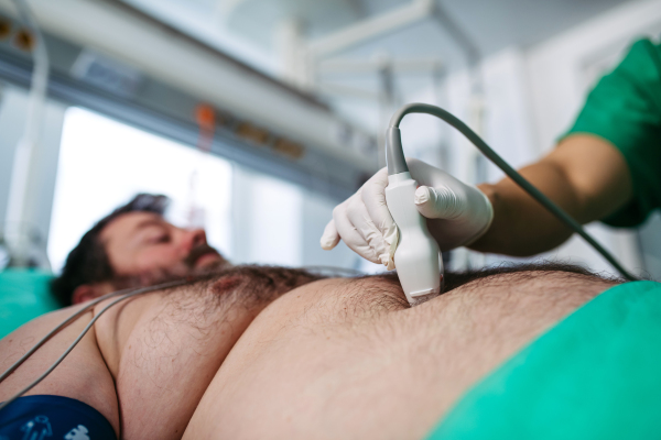 Close-up of doctor performing abdominal ultrasound on ICU patient.