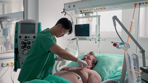 Doctor taking care of unconscious patient in hospital bed. Intensive care unit.