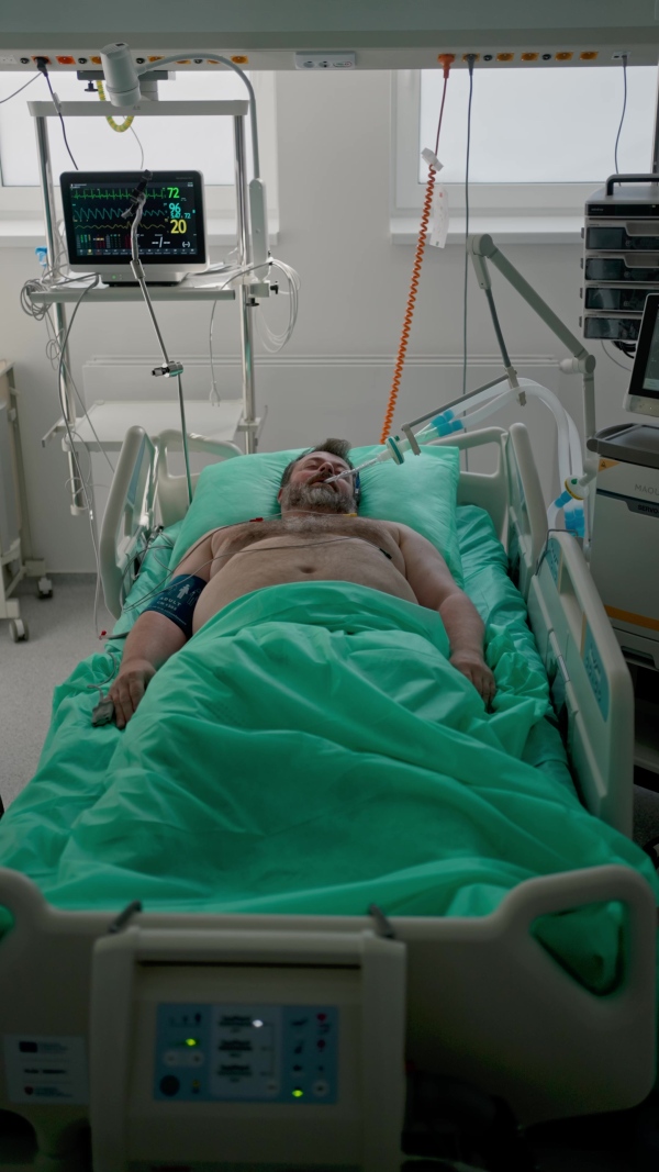 Intubated male patient lying unconscious in intensive care unit.